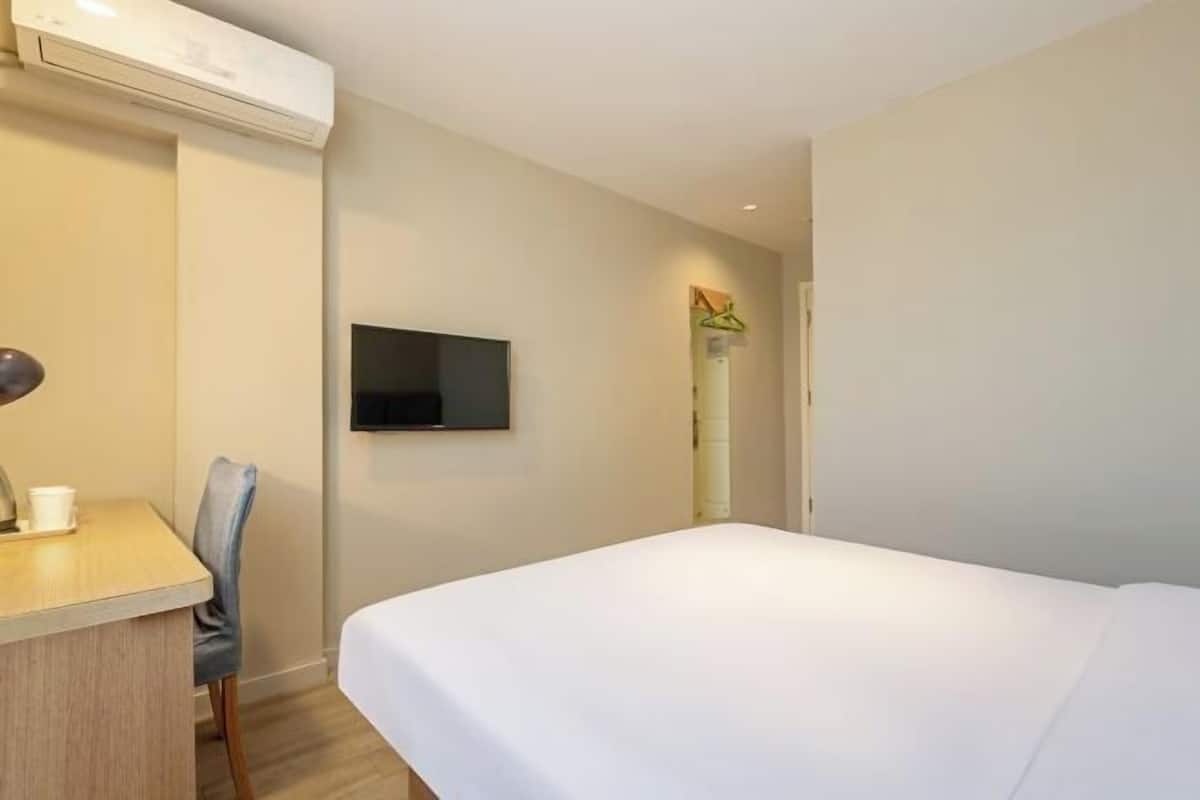 A hotel room with a bed, a desk with a chair, a television, and an air conditioning unit.