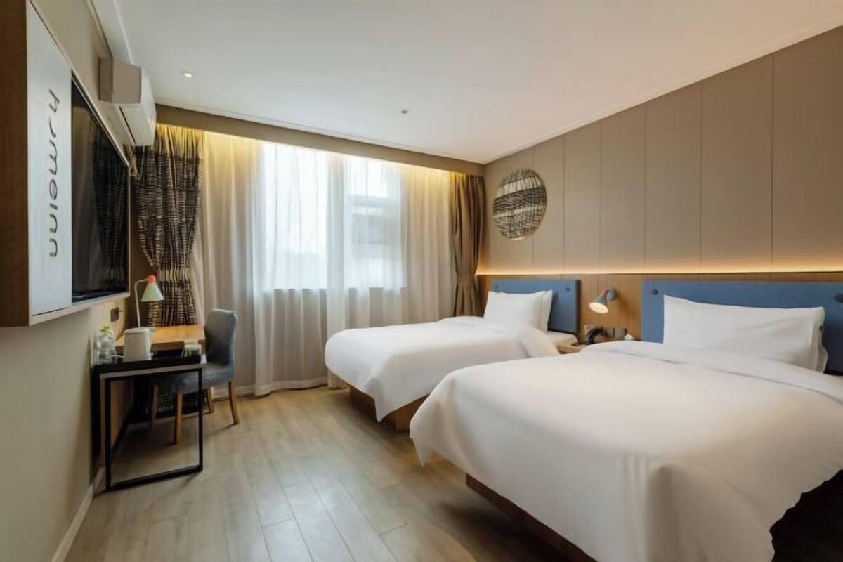 A hotel room with two beds, a desk, a chair, a TV, and a window with curtains.