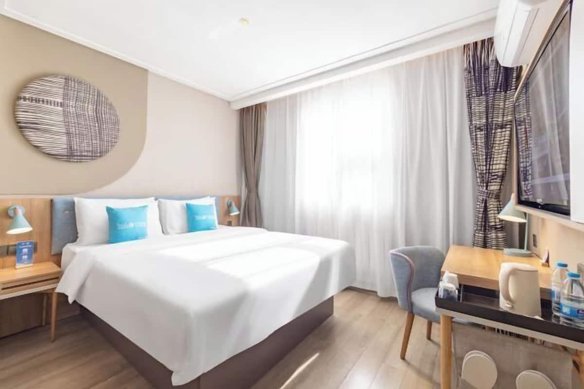 A hotel room with a bed, a desk, a chair, a TV, and a window with curtains.
