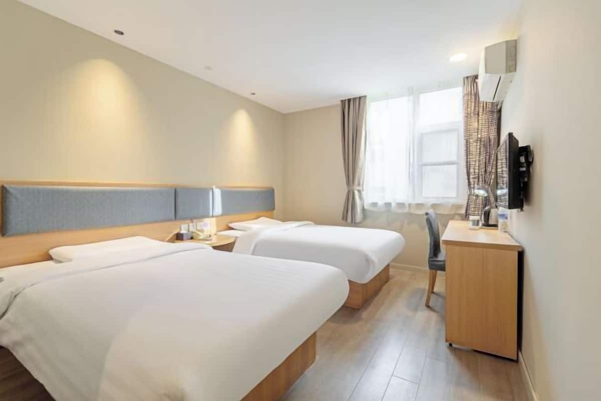 A hotel room with two beds, a desk, a chair, and a TV mounted on the wall.