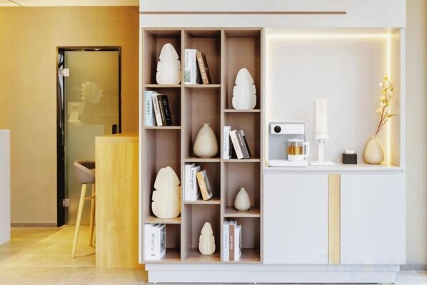 A reception area with a white reception desk, a bookshelf with decorative items, and a small seating area with a chair. - Homeinn Hotel (Weifang Xinhua Road Shengli East Street City Government Plaza) (Weifang)