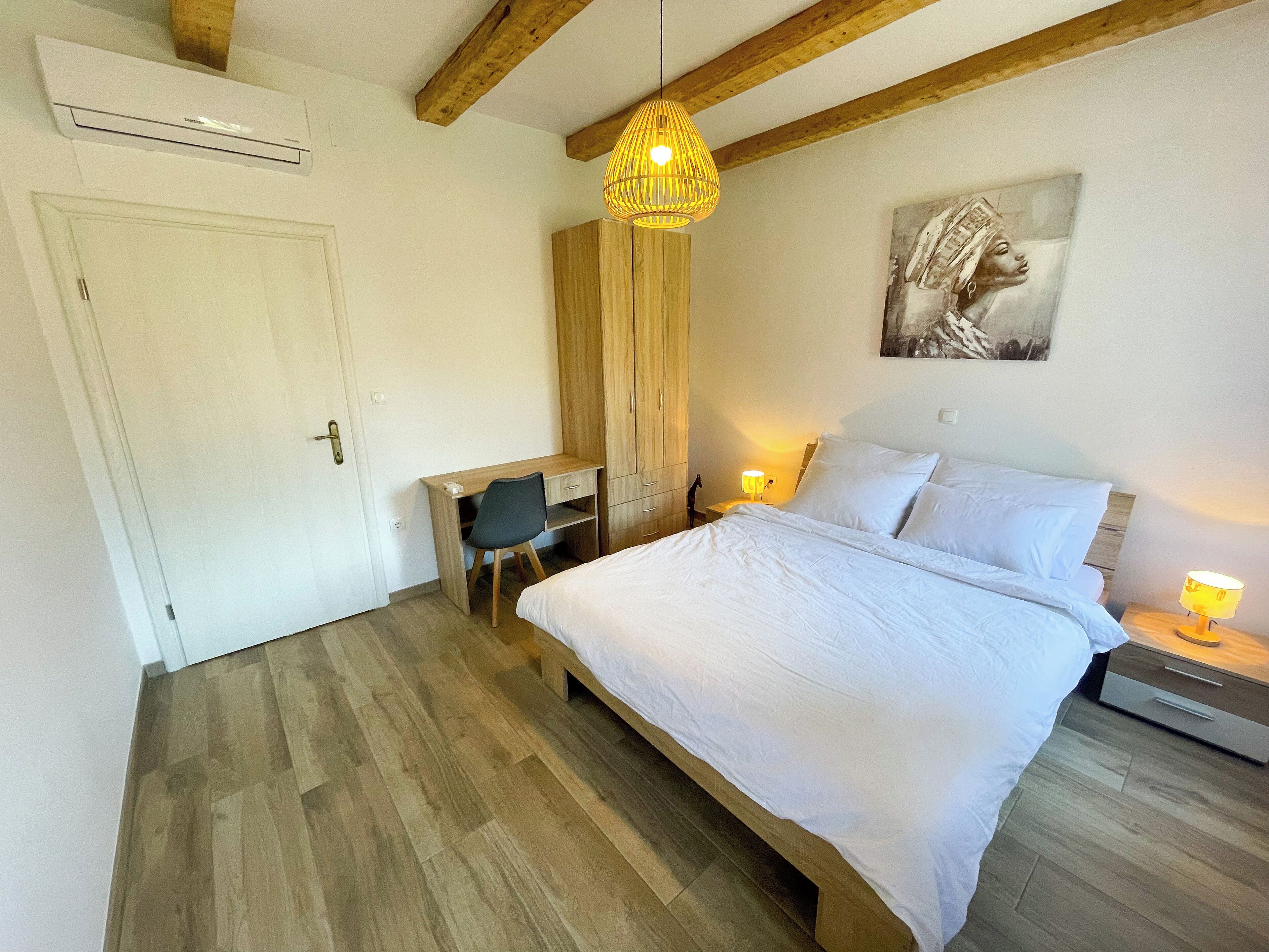 A bedroom with a bed, a desk, a chair, a wardrobe, and a hanging light fixture.
