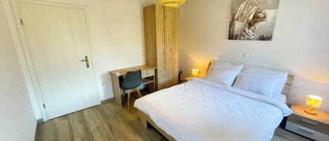 A bedroom with a bed, a desk, a chair, a wardrobe, and a hanging light fixture.