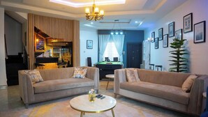 A living room with two sofas, a coffee table, a pool table, and a chandelier. - Koraf Hotels and Apartments (Abuja)