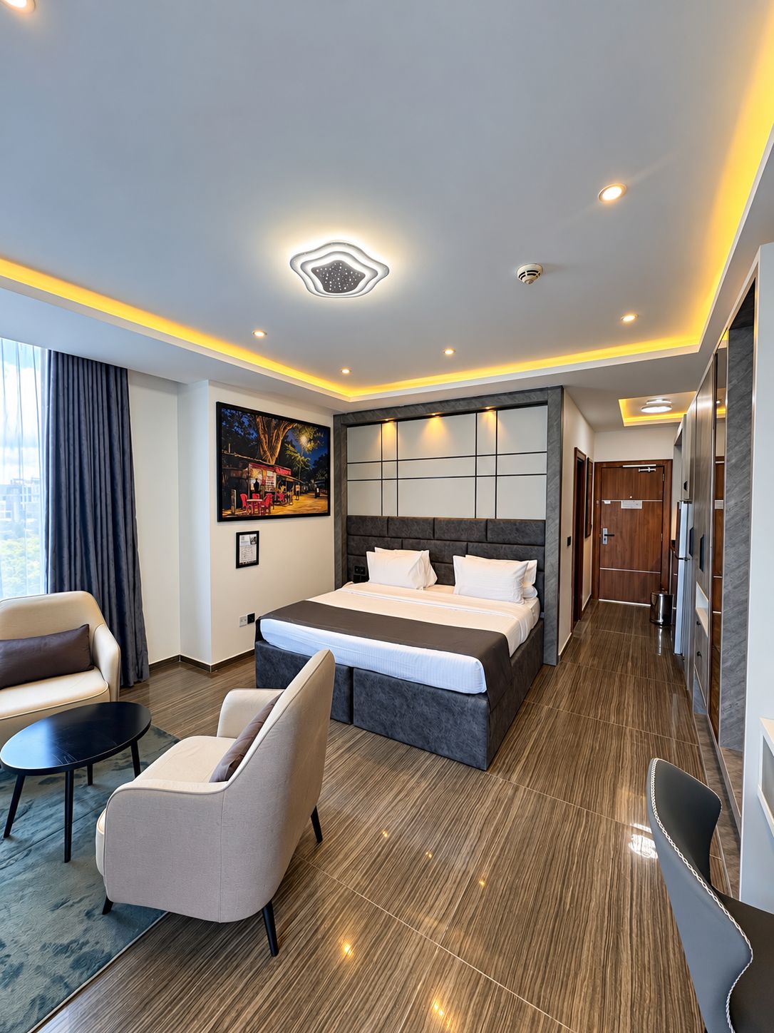A modern hotel room with a large bed, a sofa, a small table, and a painting on the wall.
