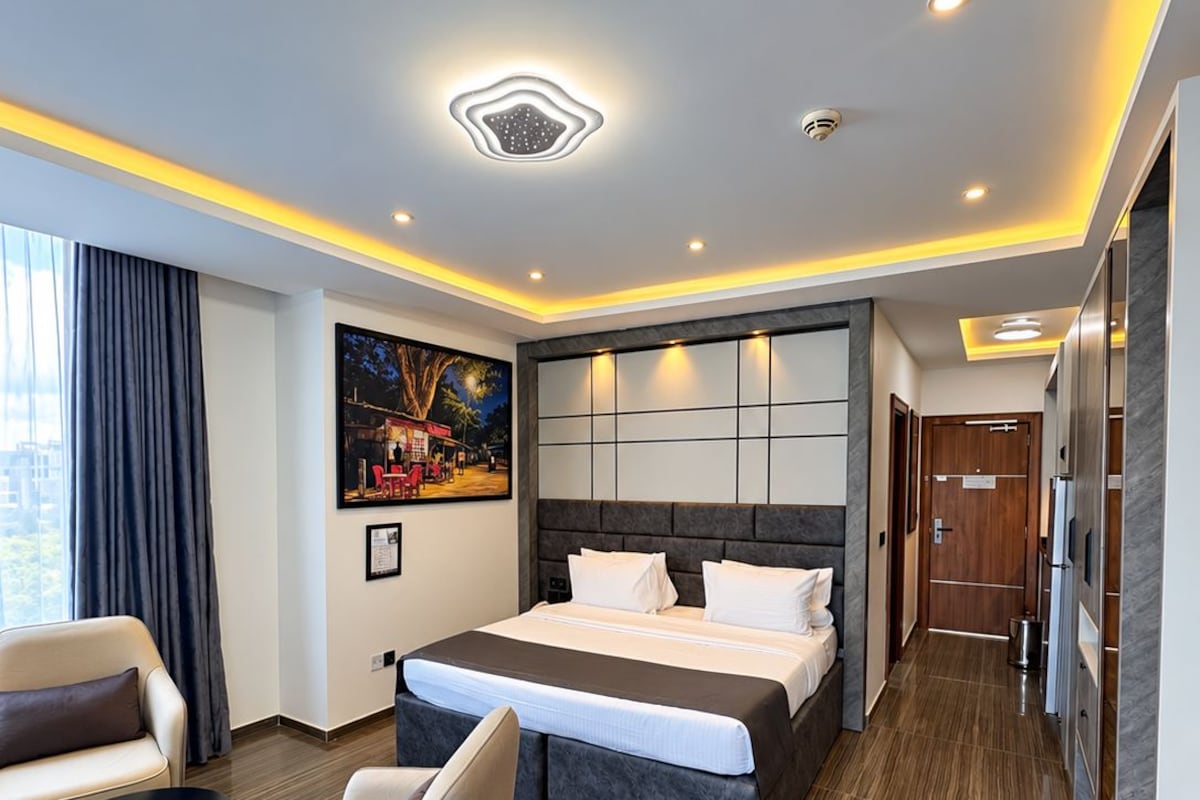 A modern hotel room with a large bed, a sofa, a small table, and a painting on the wall.
