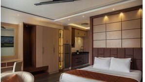 A modern hotel room with a bed, a desk, a chair, a kitchenette, and a large window. - NAF Conference Center (Abuja)