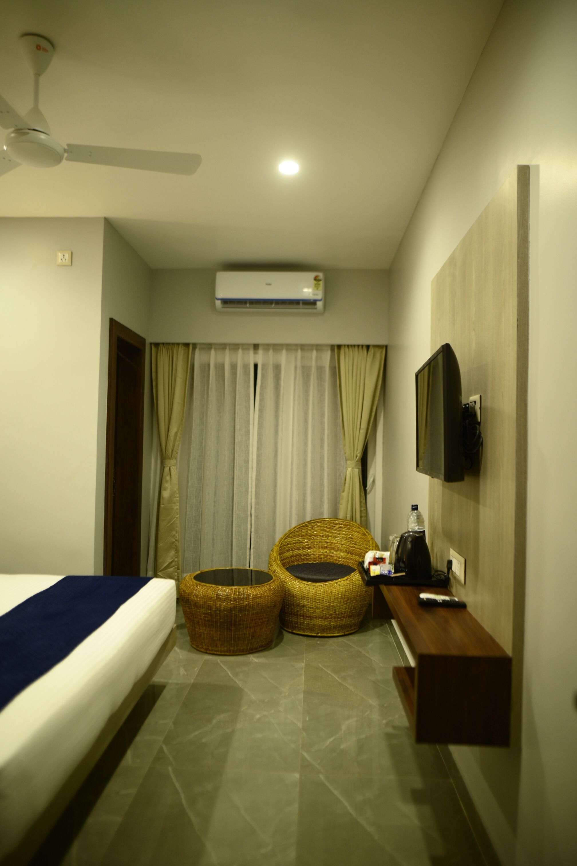 A hotel room with a bed, two wicker chairs, a TV, and a small wooden table.