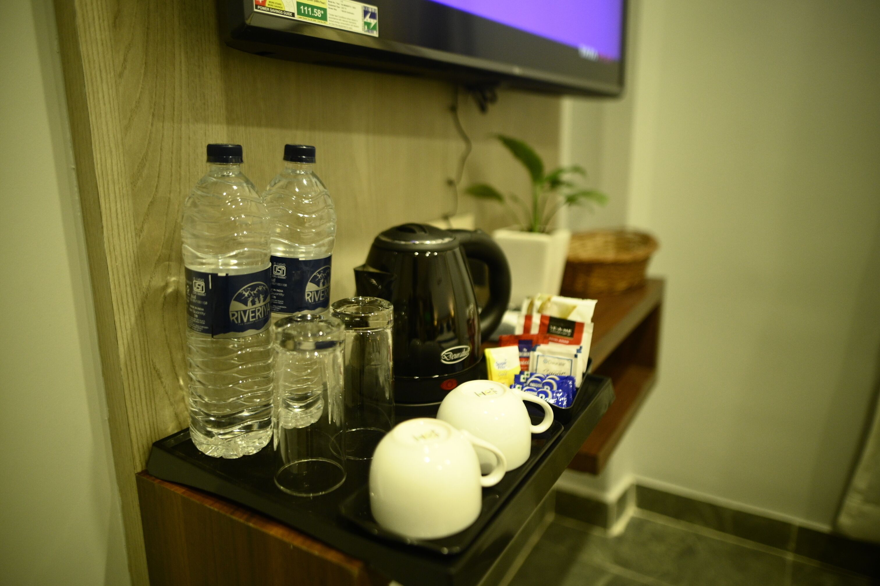 Minibar de una habitación de hotel con agua embotellada, vasos, una tetera y algunos aperitivos envasados.