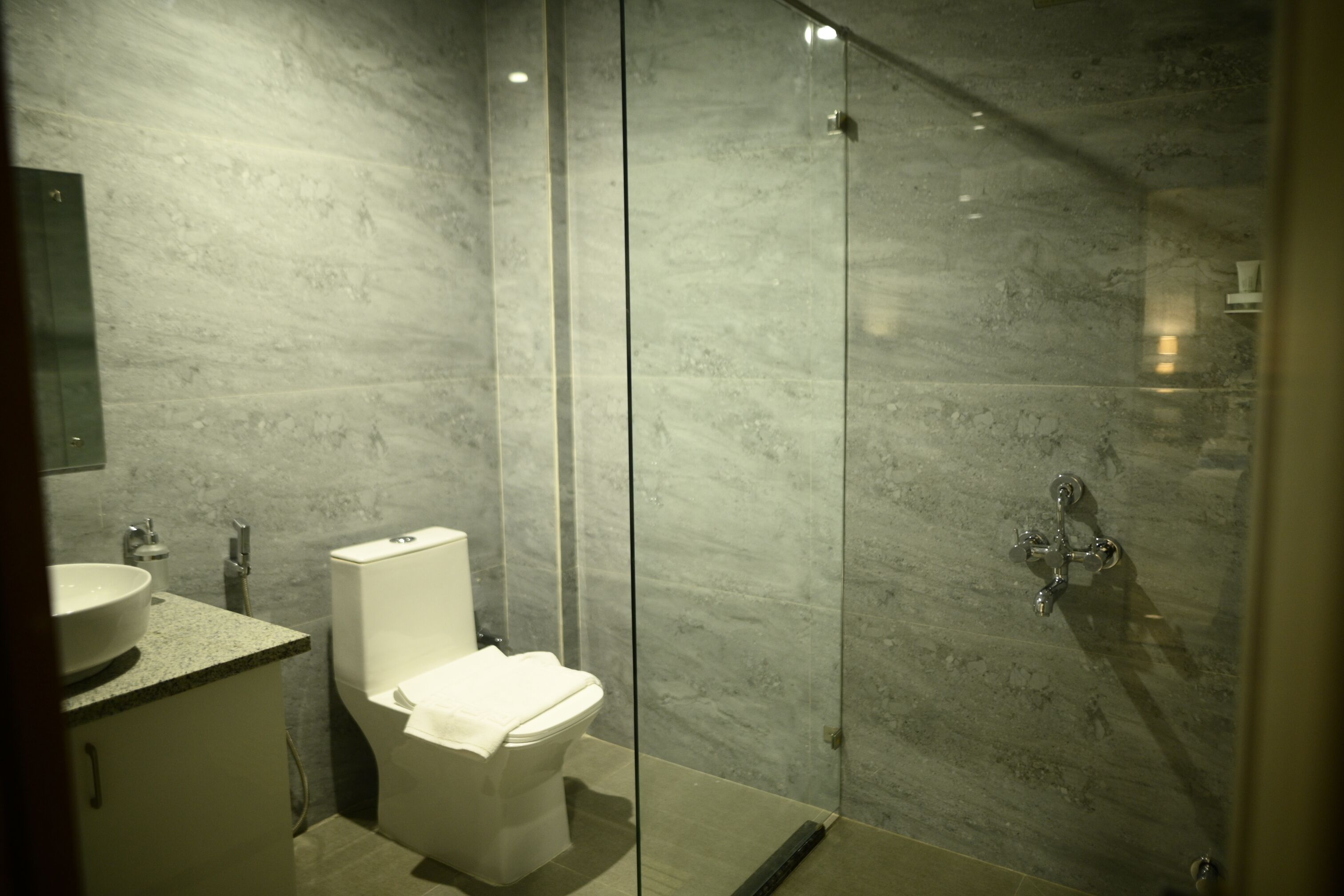 Un baño moderno con cabina de ducha de vidrio, inodoro blanco y encimera de granito con lavamanos.