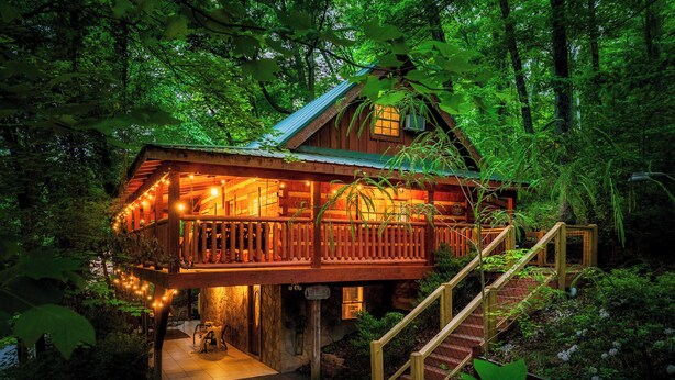 Une cabane en bois dotée d’un balcon, entourée d’une forêt dense.