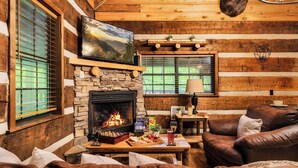 L’intérieur chaleureux d’un chalet avec une cheminée, des murs en bois, un canapé confortable et une table à manger où sont disposés des en-cas.