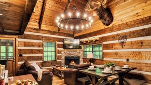 L’intérieur d’un chalet rustique, avec une cheminée, des murs en bois, un canapé en cuir, une table à manger et une tête de cerf accrochée au mur.