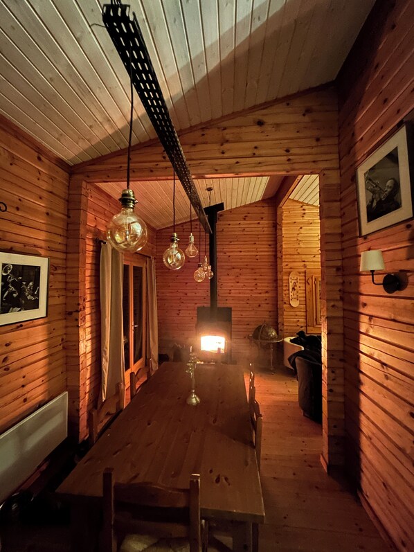 Een houten interieur met een lange eettafel, hangende lampen en een zichtbare open haard.