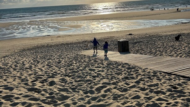 Ein sandiger Strand mit Fußabdrücken und einem hölzernen Steg.