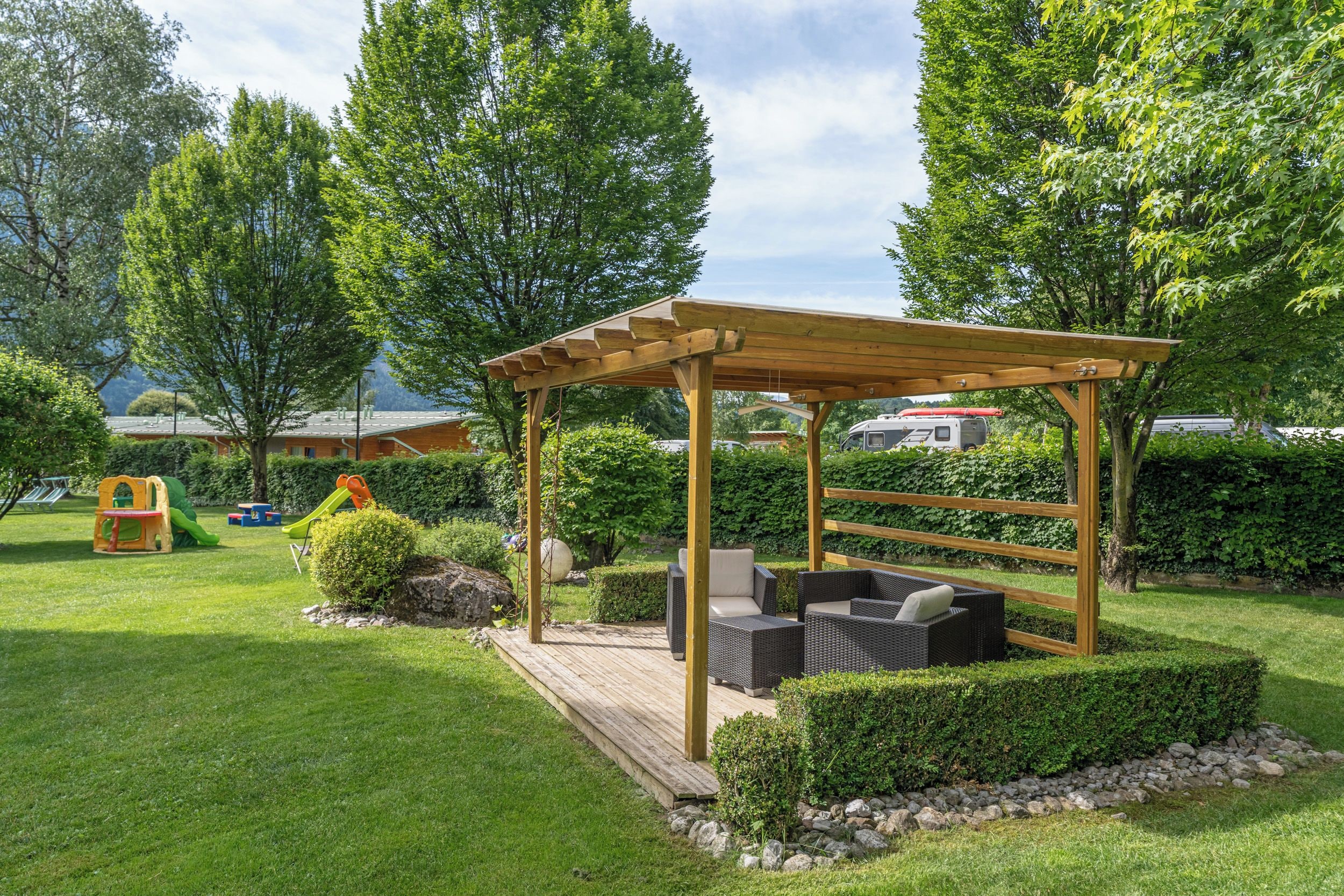 A wooden pergola with seating, surrounded by a well-maintained lawn and hedges.