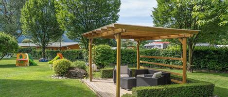 A wooden pergola with seating, surrounded by a well-maintained lawn and hedges.
