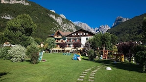 Een hotel met een berg op de achtergrond, een verzorgd gazon en buitenspeeltoestellen.
