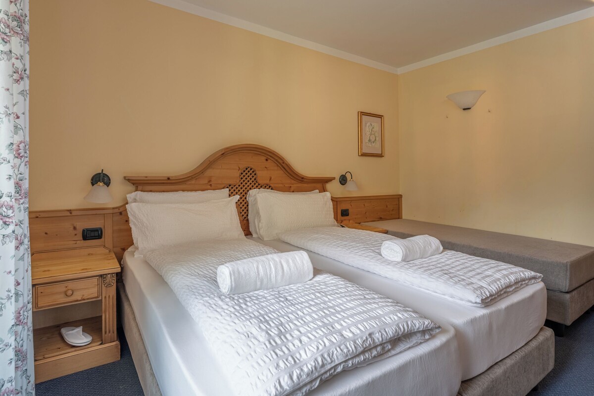A hotel room with two beds, wooden headboards, bedside tables, and a nightstand.