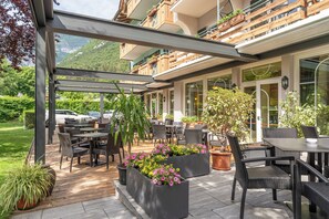 Un espace extérieur aménagé en terrasse, avec des tables et des chaises, entouré de plantes en pot et offrant une vue sur une montagne.