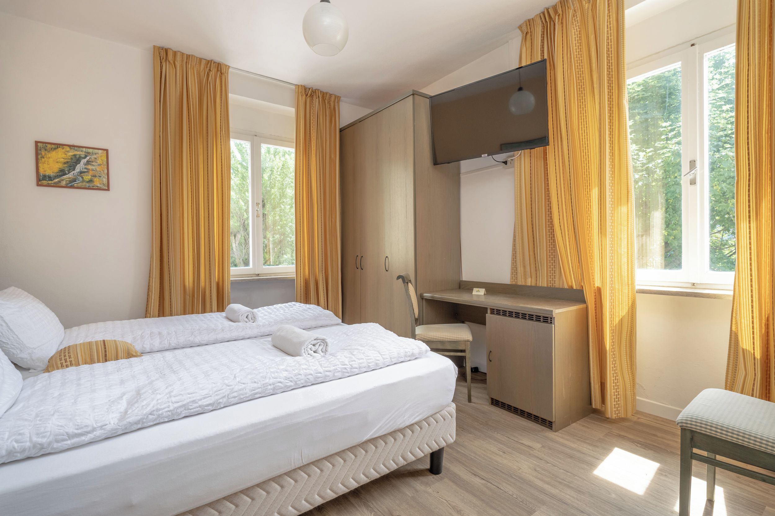 Ein Hotelzimmer mit Bett, Schreibtisch und einem großen Fenster mit Vorhängen.
