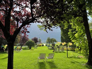 A park with grass, trees, and outdoor seating. - Garden Hotel Bellariva (Molveno)