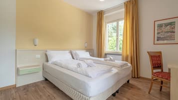 Une chambre d’hôtel avec un lit, une chaise, une fenêtre avec des rideaux, un luminaire fixé au mur et un tableau.