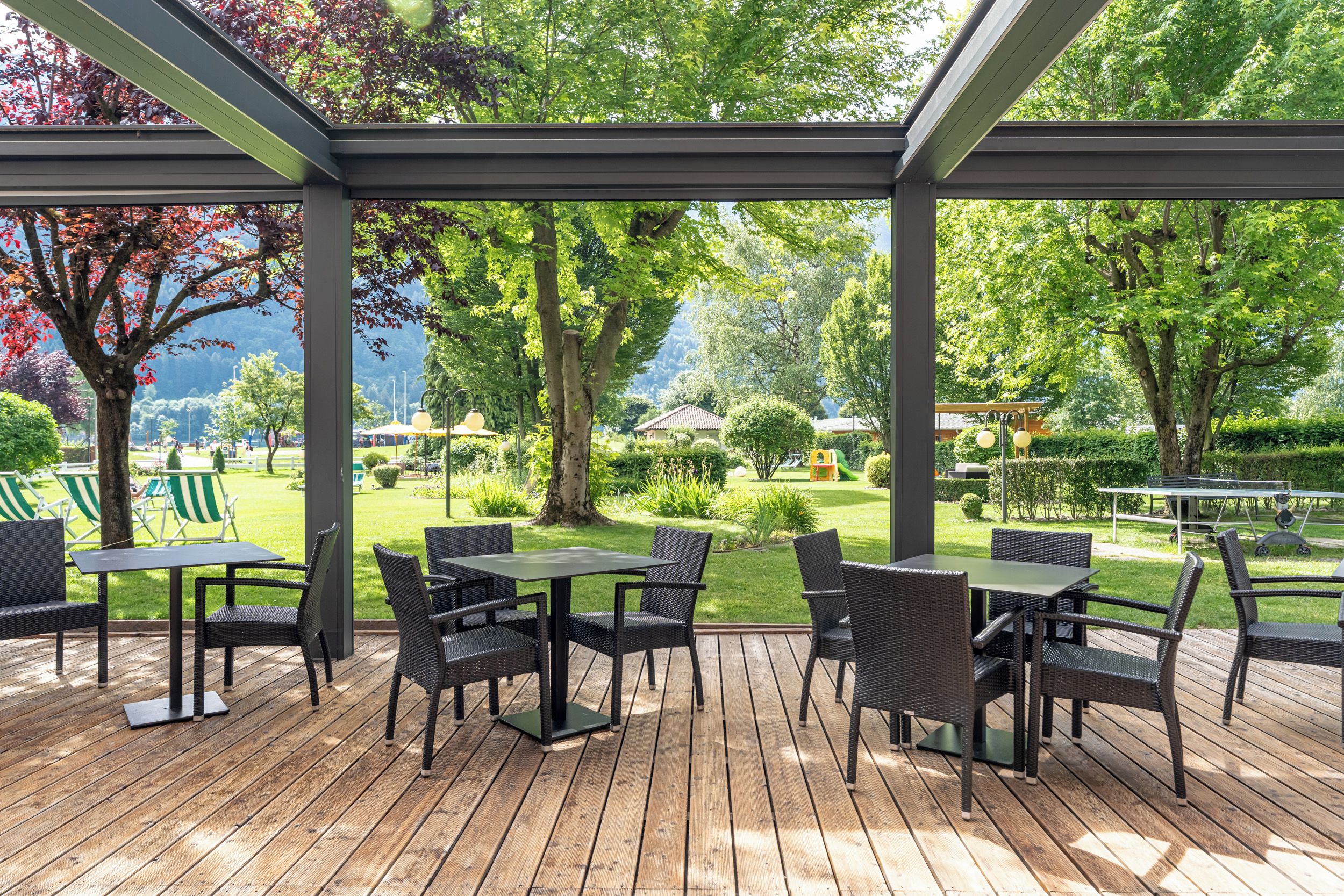 An outdoor patio with tables and chairs, surrounded by greenery and trees.