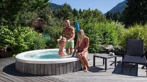 Een hottub omringd door weelderige begroeiing en een terras met buitenmeubilair.