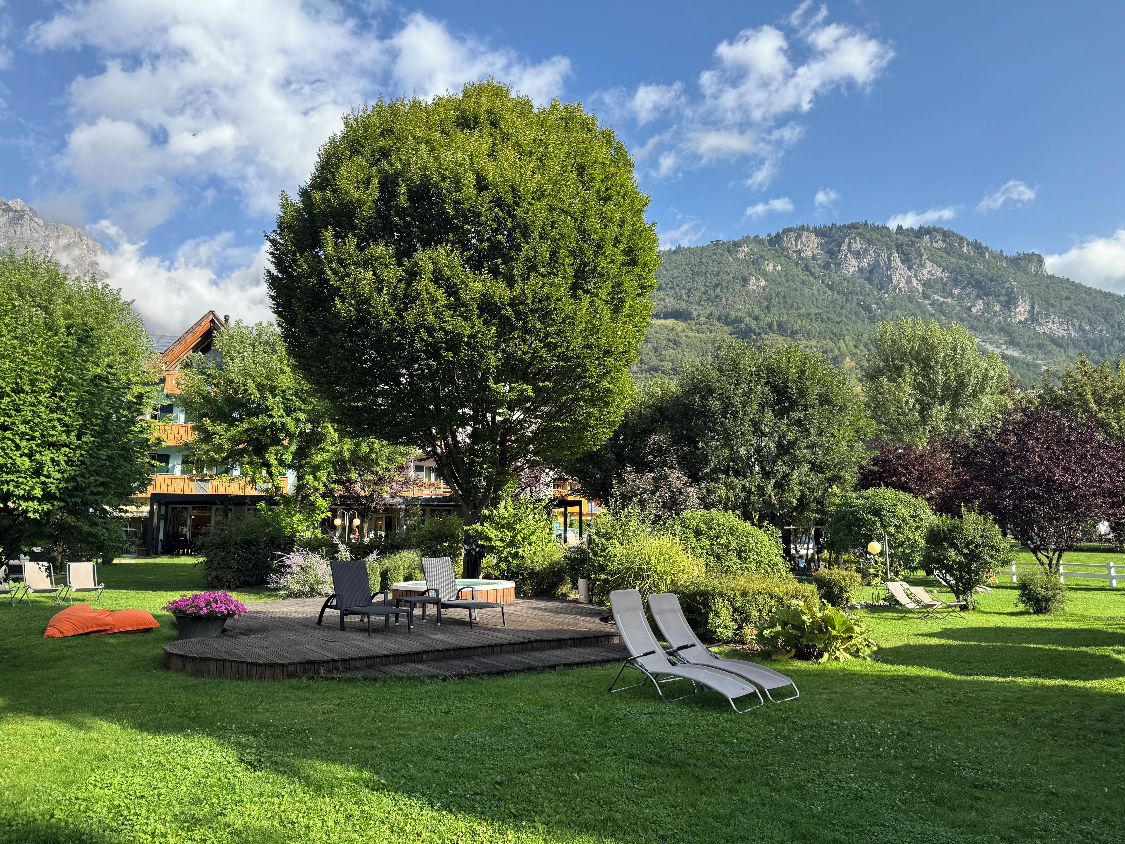 A lush garden with a large tree, outdoor seating, and a mountain backdrop.