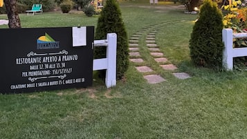 A garden hotel with a sign indicating an open-air restaurant, a mountain backdrop, and a well-maintained lawn.