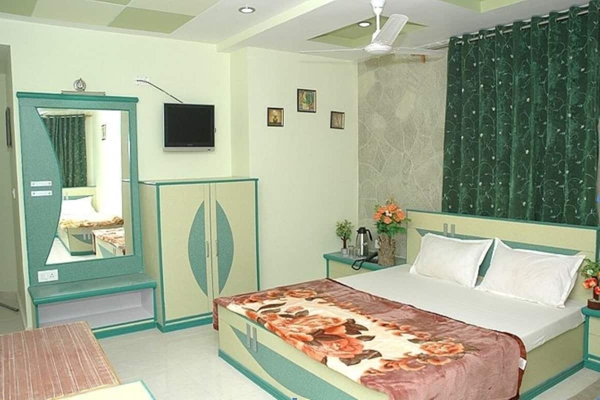 A bedroom with a bed, a nightstand, a mirror, a television, and a green curtain.