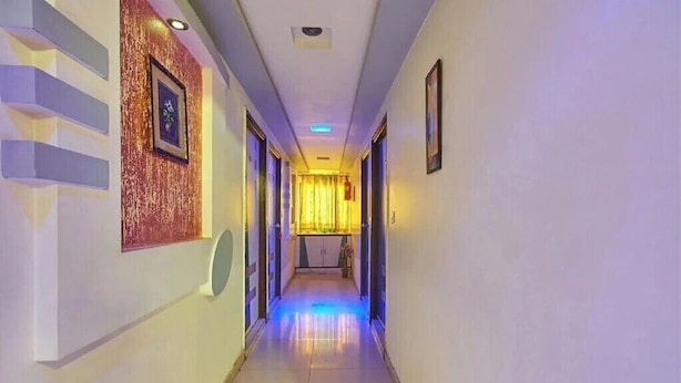 A hotel hallway with a reflective floor, framed artwork on the walls, and a door at the end. - Hotel Liberty (Ahmedabad)