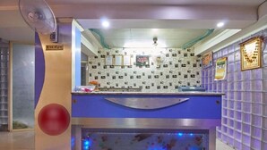 A reception area with a counter, a wall-mounted fan, and a decorative wall with patterned tiles. - Hotel Liberty (Ahmedabad)