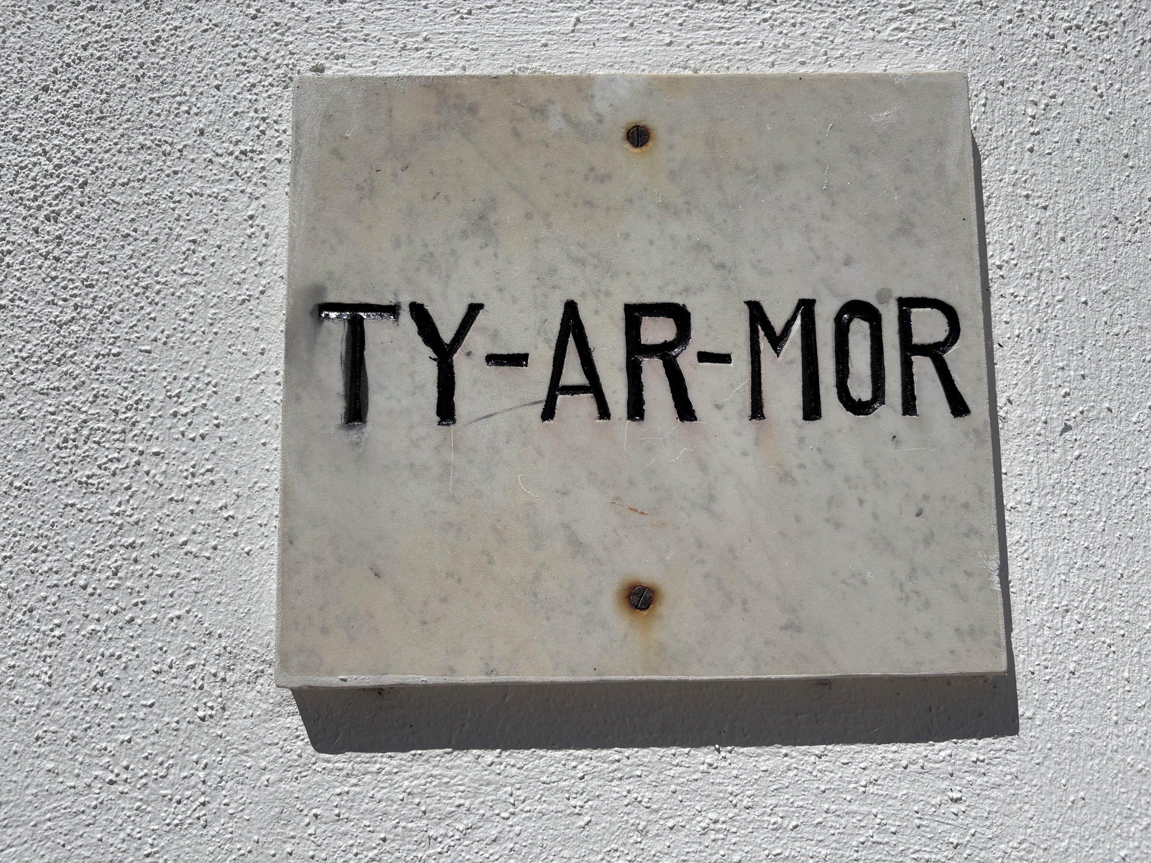 A sign with the inscription "TY-AR-MOR" on a textured wall.