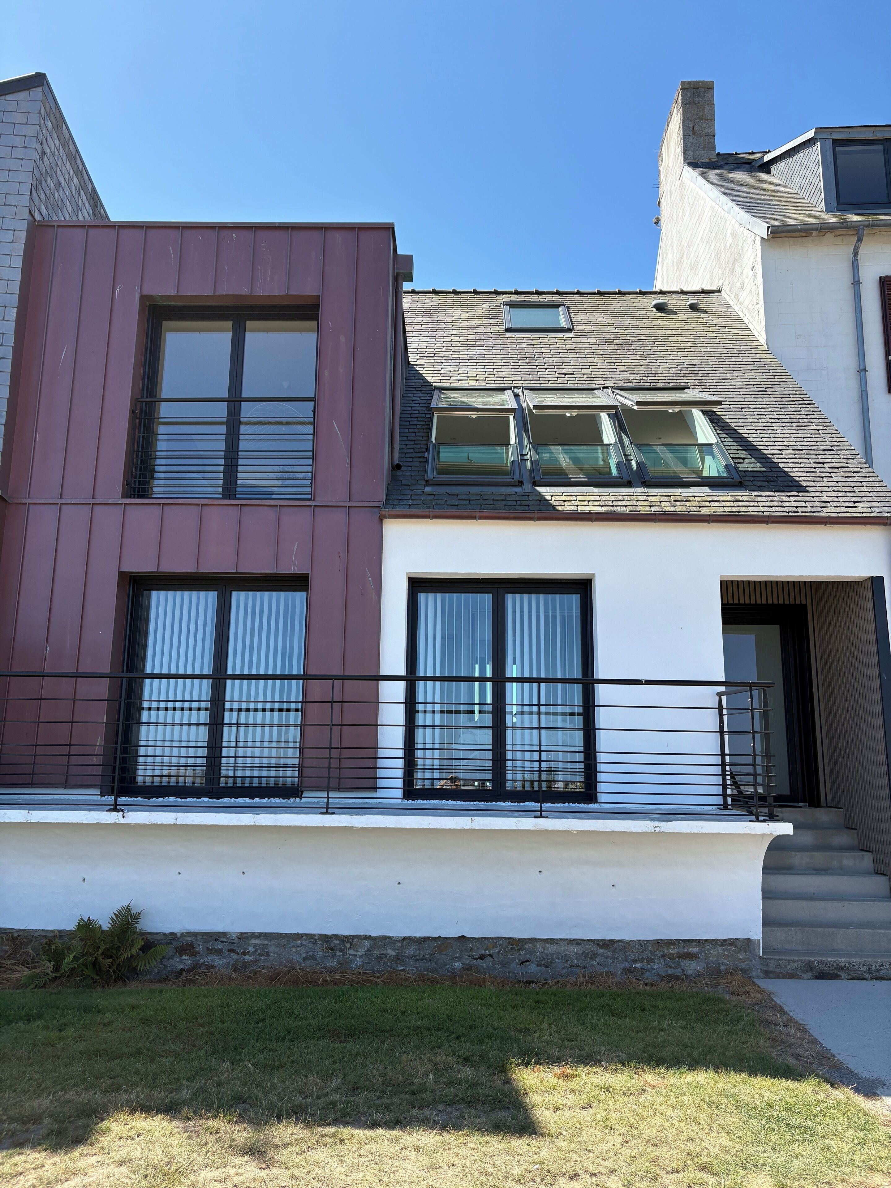 Een modern herenhuis met twee verdiepingen, een plat dak, grote ramen en een kleine voortuin.