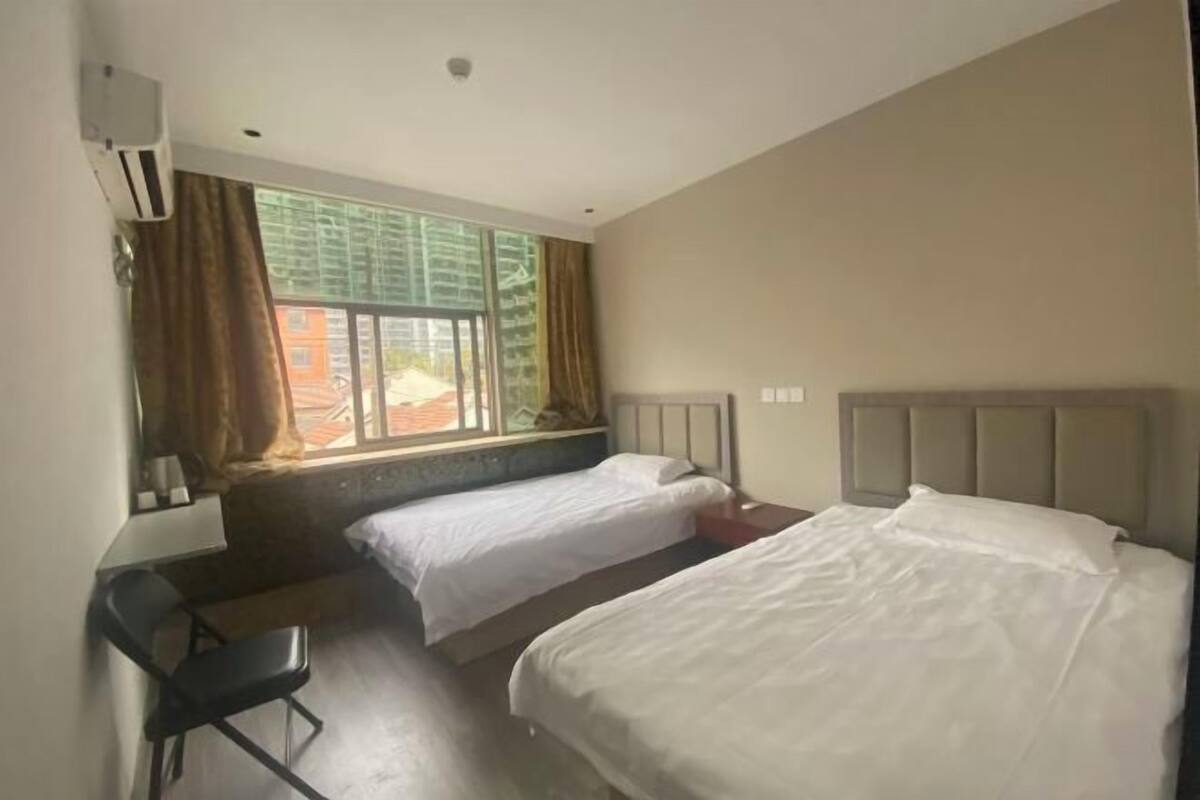 A hotel room with two beds, a desk, and a window with curtains.