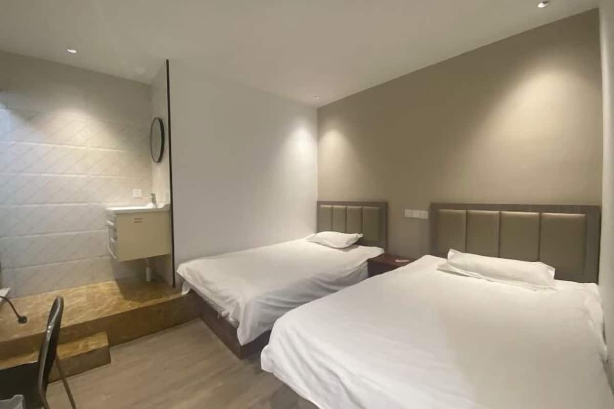 A hotel room with two beds, a small bedside table, a mirror, and a built-in bench with a chair.