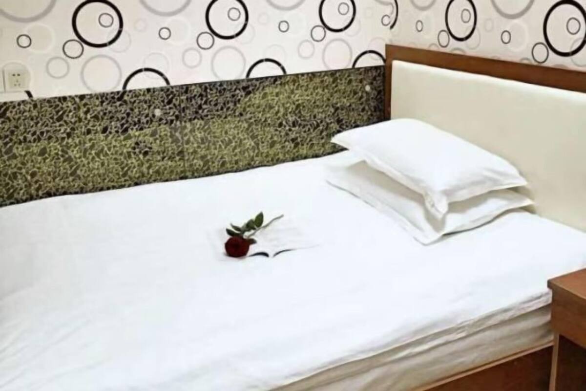 A bed with a white sheet, a single red rose, and a white pillow.