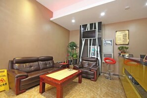 A hotel lobby with a leather sofa, a wooden coffee table, a reception desk, and a plant. - Yijia Business Hotel (Shanghai)