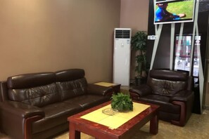 A living room with a brown leather sofa, a wooden coffee table, and a flat-screen TV mounted on the wall. - Yijia Business Hotel (Shanghai)