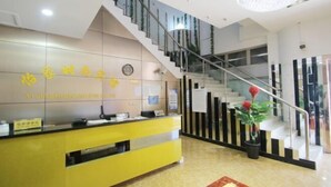A reception area with a yellow counter, a staircase with a glass railing, and a clock on the wall. - Yijia Business Hotel (Shanghai)