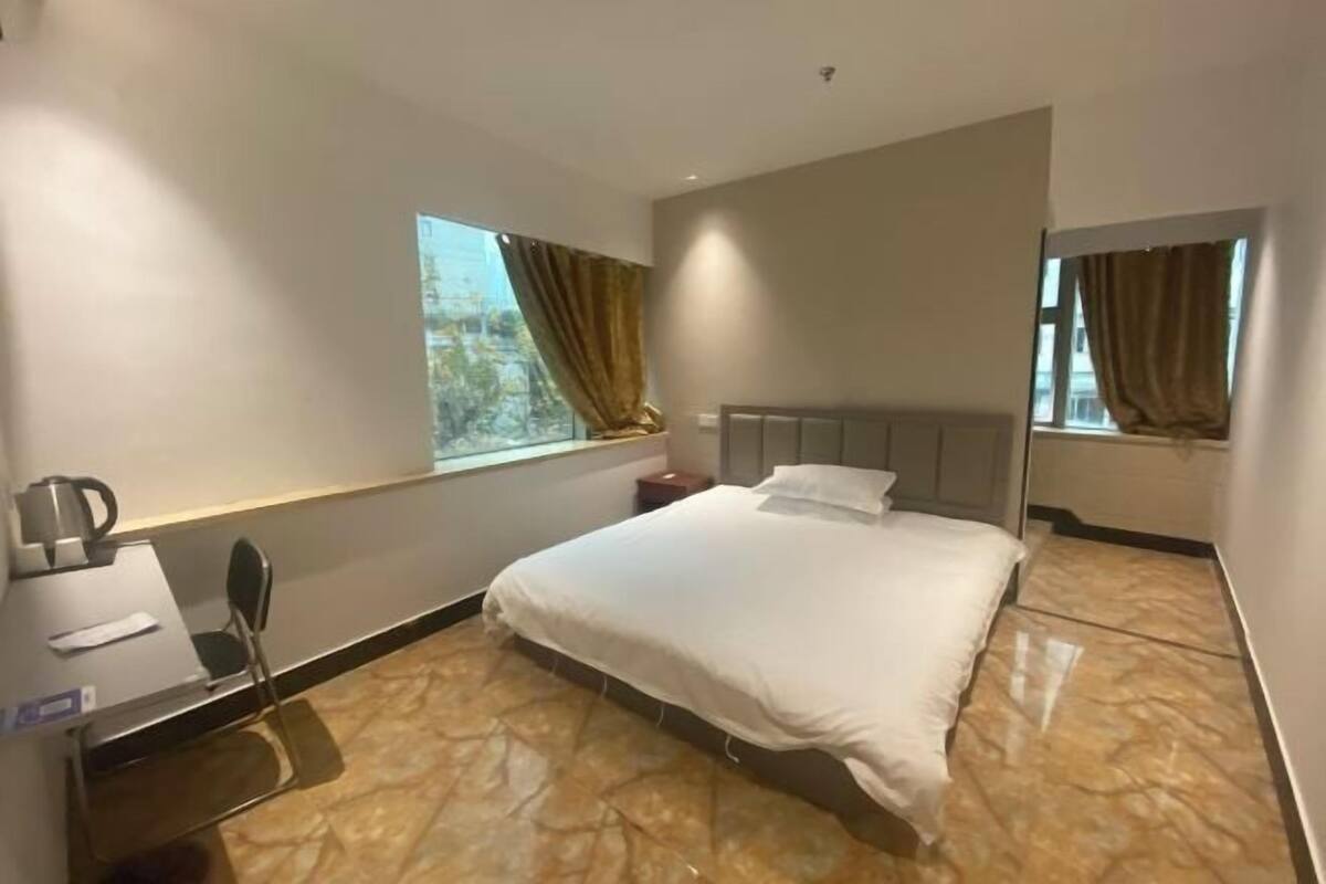A hotel room with a bed, a desk, a chair, a nightstand, and a window with curtains.