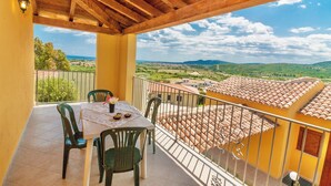 Un balcón con mesa y sillas, con vistas a un paisaje pintoresco con edificios y colinas.