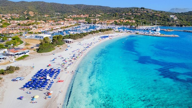 Un pueblo costero con playa, aguas azules cristalinas y un puerto deportivo.