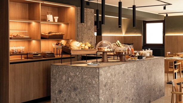 Un bar à petit-déjeuner moderne, doté d’étagères en bois et de plans de travail en marbre, où l’on trouve une variété d’aliments et un espace dédié au café.