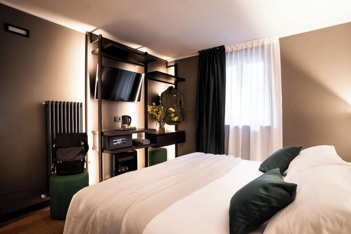 Habitación de hotel con una cama grande, un televisor de pantalla plana en la pared, un escritorio con una silla y un radiador.