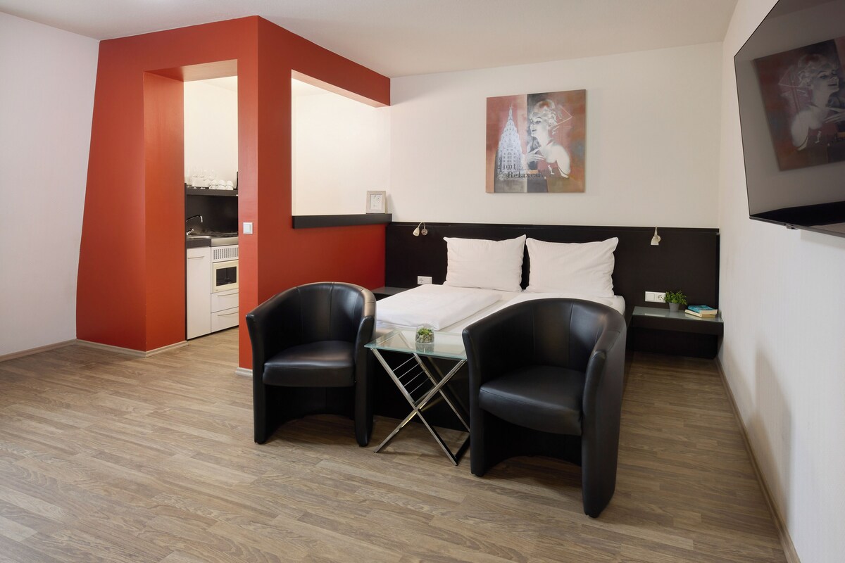 A modern room with a bed, two chairs, a small table, and a painting on the wall.