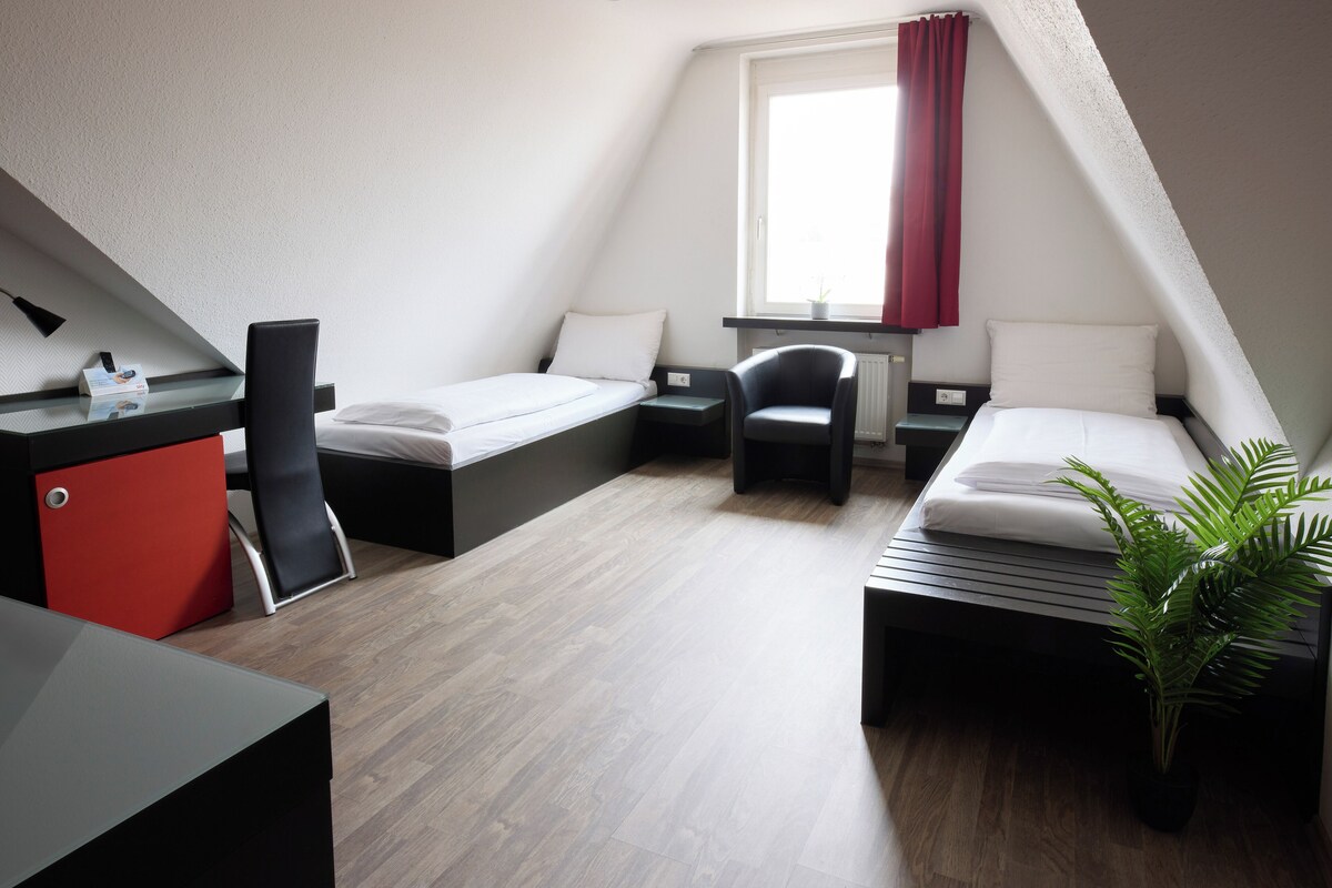A modern, compact room with two beds, a desk, and a chair.