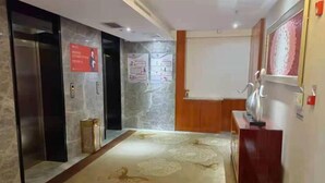 A hotel lobby with a marble wall, a wooden reception desk, and a patterned carpet. - Pingliang Rongting Hotel (Pingliang)
